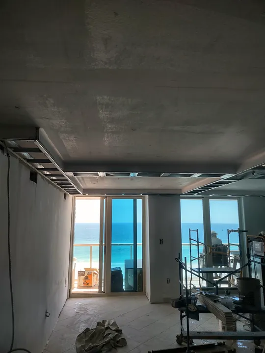Gulf-front condo mid-remodel: new metal ceiling framing and Gulf views through the balcony doors
