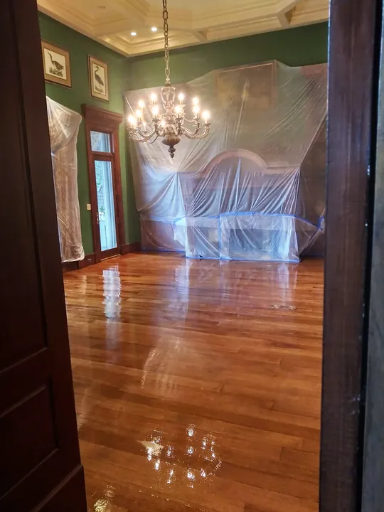 Refinished hardwood floor with a high-gloss finish in a dining room with green walls and a chandelier