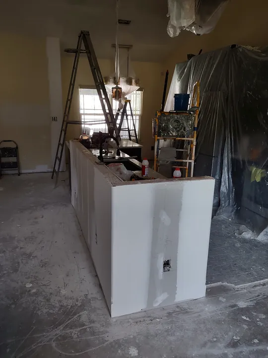 Kitchen island wrapped in new drywall with seams taped, room masked off for work
