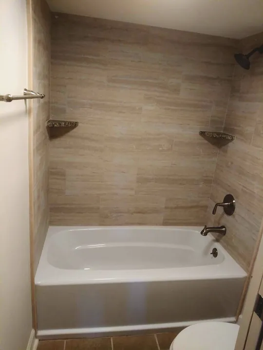 Tub surround finished in large-format beige tile with corner shelves